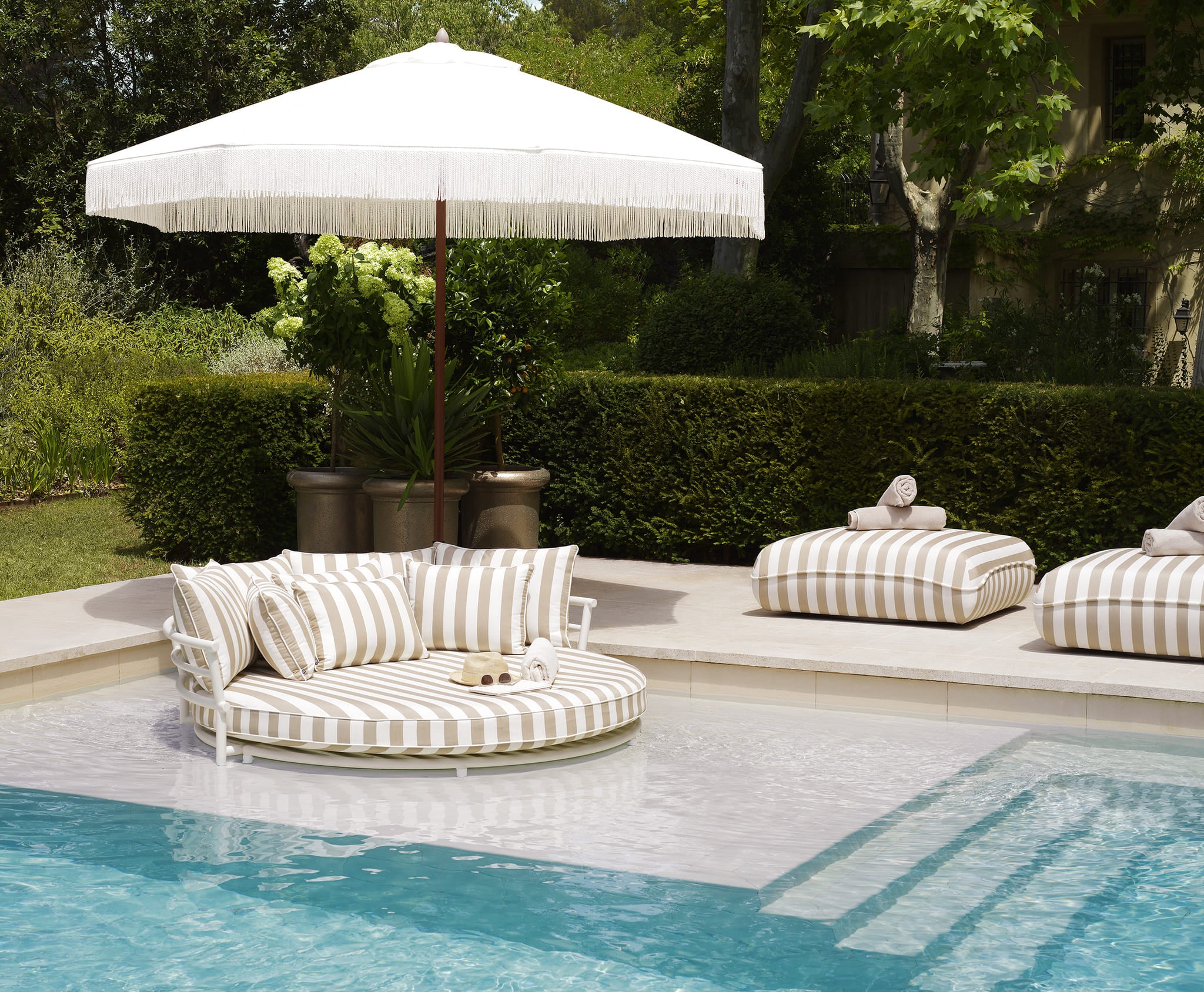 Rundes Eichholtz Daybed mit weißen und beigen Streifen am Pool unter elegantem weißen Sonnenschirm im luxuriösen Garten.