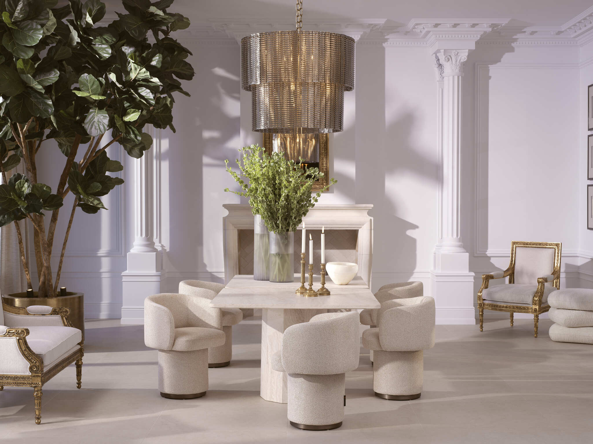 Eichholtz Esszimmer mit Travertin-Esstisch und gepolsterten Stühlen aus der The Met Kollektion, ergänzt durch klassische Sessel, einen Kronleuchter und Wandgestaltung mit Säulen im Showroom in Wien
