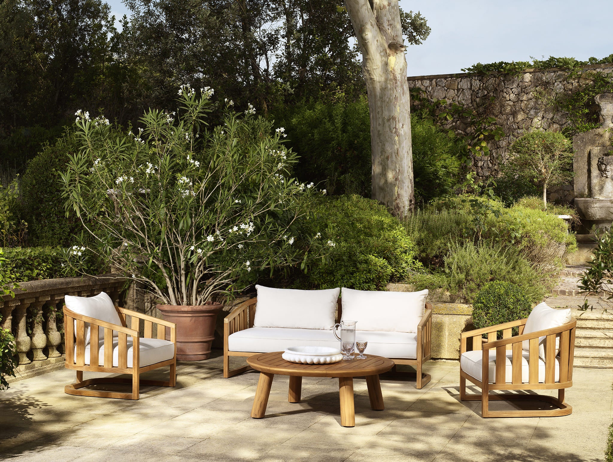 Moderne Eichholtz Gartenlounge aus Holz mit weißen Kissen und Couchtisch auf eleganter Natursteinterrasse.