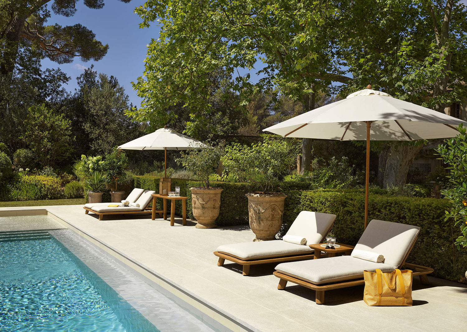 Hochwertige Eichholtz Sonnenliegen mit weißen Polstern und Sonnenschirmen am Pool in grünem Gartenambiente.