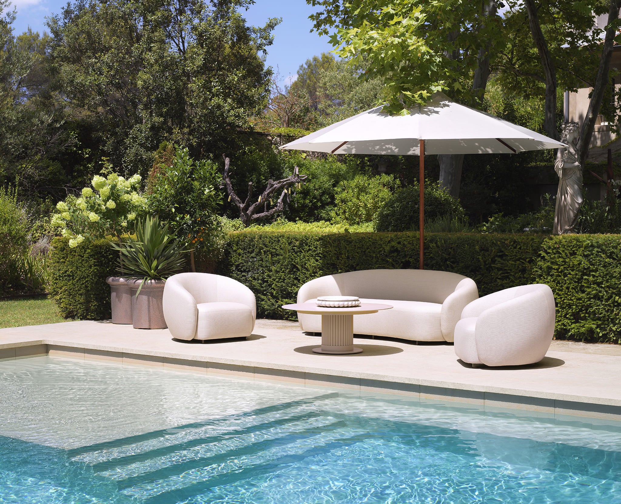 Zeitlose Eichholtz Outdoor Lounge mit rundem Sofa und Sesseln in Cremeweiß neben Pool.