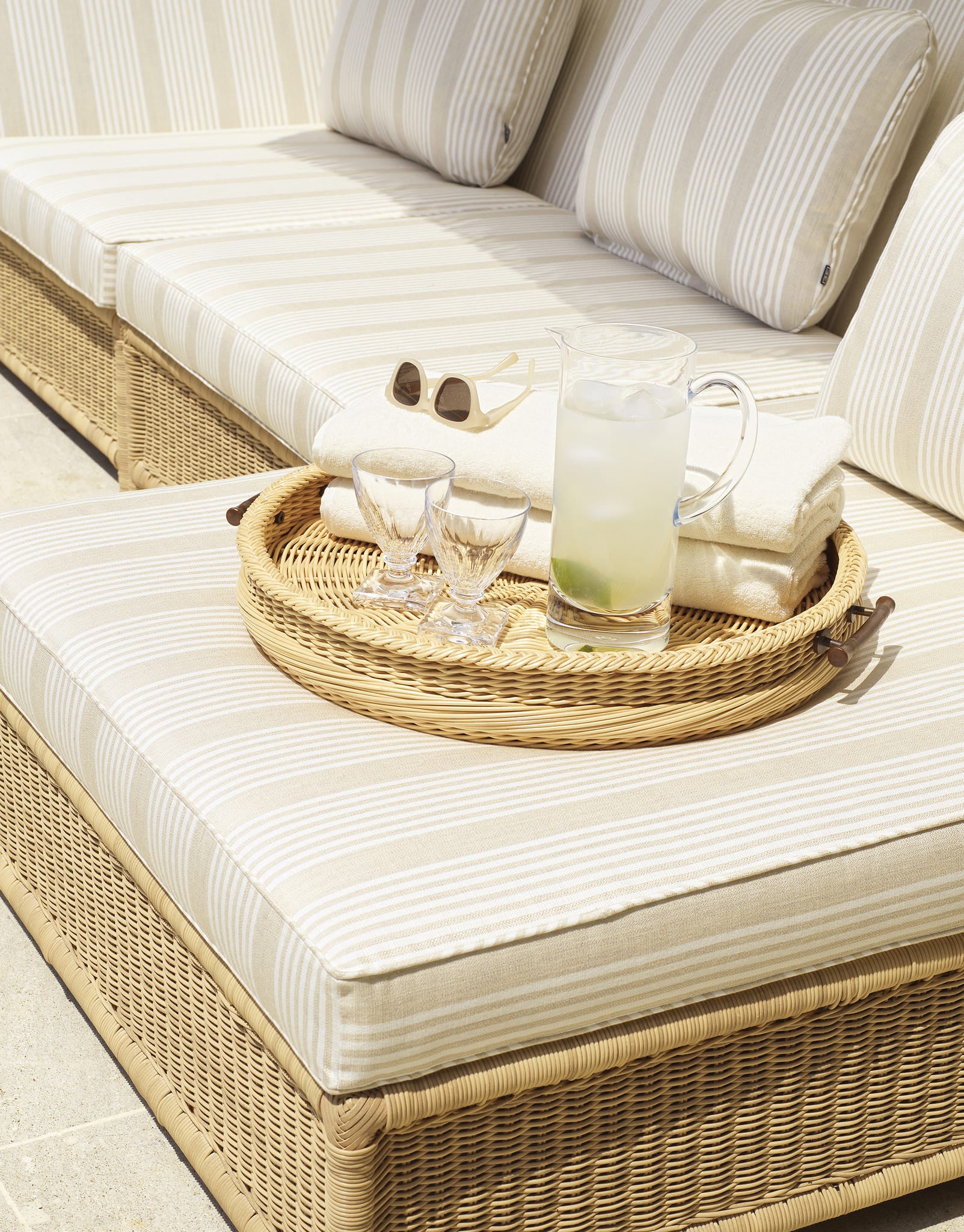 Detailaufnahme eines Eichholtz Outdoor Sofas mit Rattan-Tablett, Gläsern und erfrischender Limonade im Sonnenschein.
