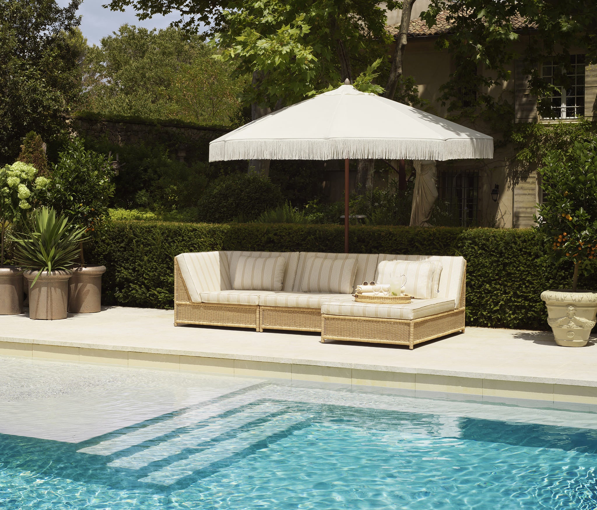 Großzügiges Eichholtz Outdoor Sofa mit Rattanoptik und gestreiften Polstern am Pool in eleganter Gartenumgebung.